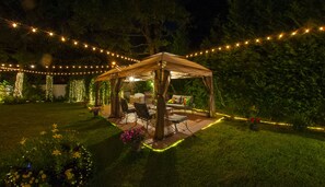 A covered outdoor seating area with string lights, a table, and chairs. - 4 BR. 2 BTH, HOT TUB, MINS TO JONES BEACH, MINS TO RIVIERA WALK TO TRAIN TO NYC (Massapequa)