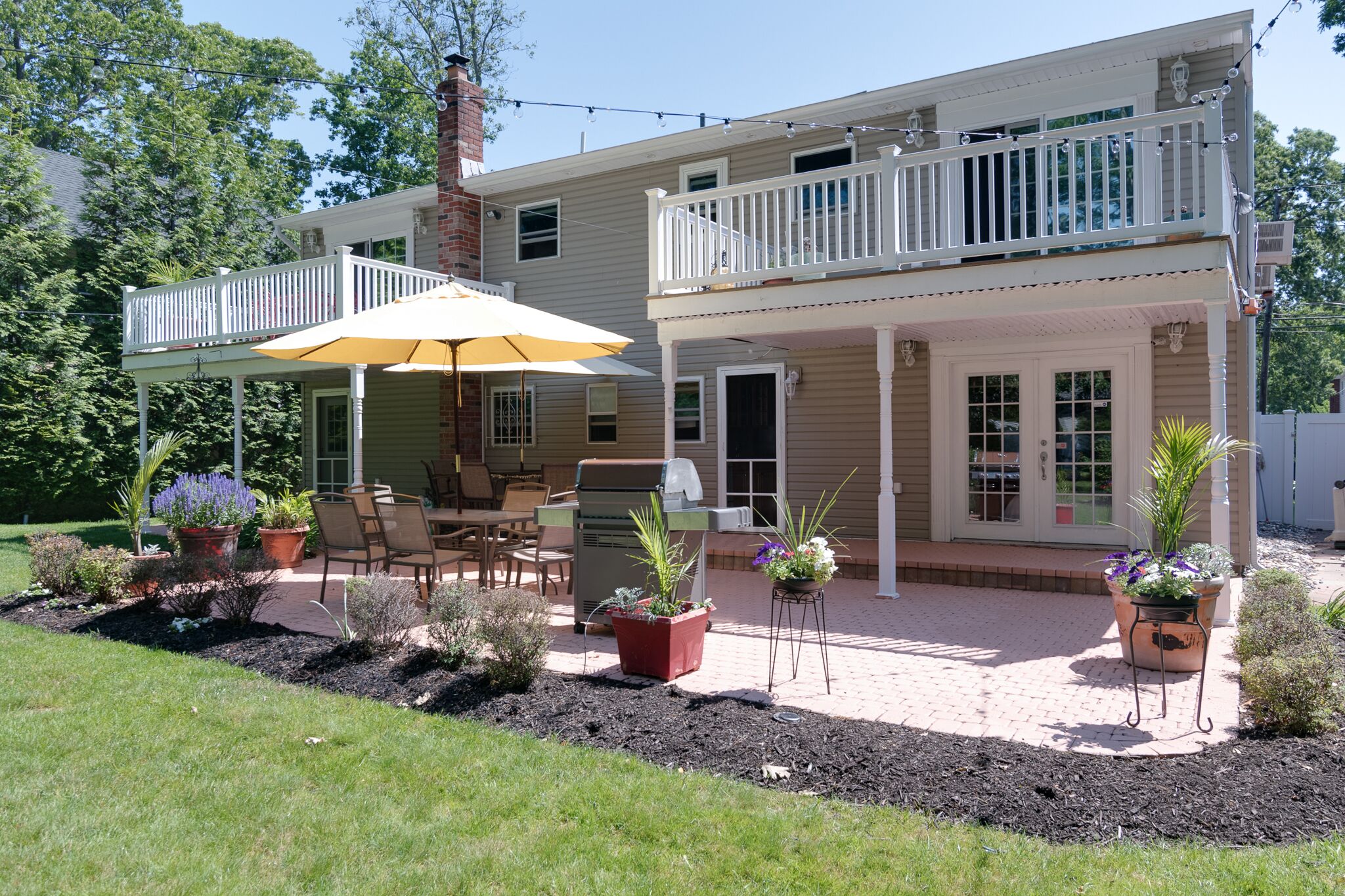 A two-story house with a covered patio, outdoor furniture, and potted plants.