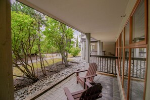 A covered outdoor area with a wooden bench and a chair, surrounded by trees and a stone pathway. - Stoney Creek Northstar 14 (Whistler)