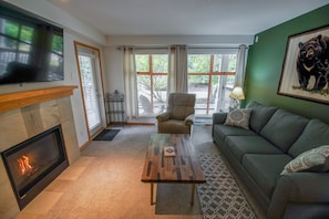 A living room with a fireplace, a sofa, a coffee table, and a television. - Stoney Creek Northstar 14 (Whistler)