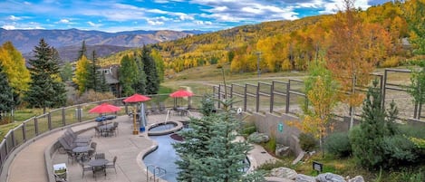 A patio area with outdoor seating, a small pool, and a view of autumn foliage and mountains.