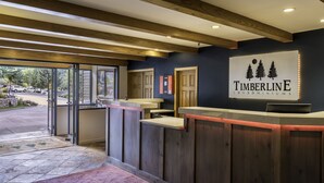 A reception area with a wooden reception desk, a sign reading "Timberline Condominiums," and a view of the outside through glass doors. - 🌲Timberline 116 Studio Deluxe ~ Hot Tub~Pool~WiFi~Ski-in/out~Local Shuttle🌲 (Snowmass Village)