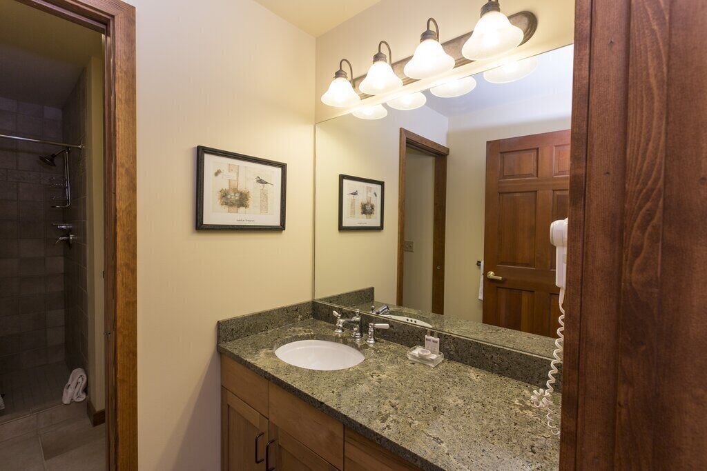 A bathroom with a granite countertop sink, a large mirror, and a shower area.
