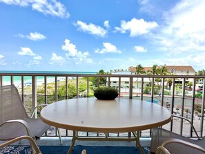 Un balcón con mesa y sillas, con vista a una playa y una zona residencial.