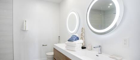 A modern bathroom with a white vanity, two illuminated mirrors, and a shower area.
