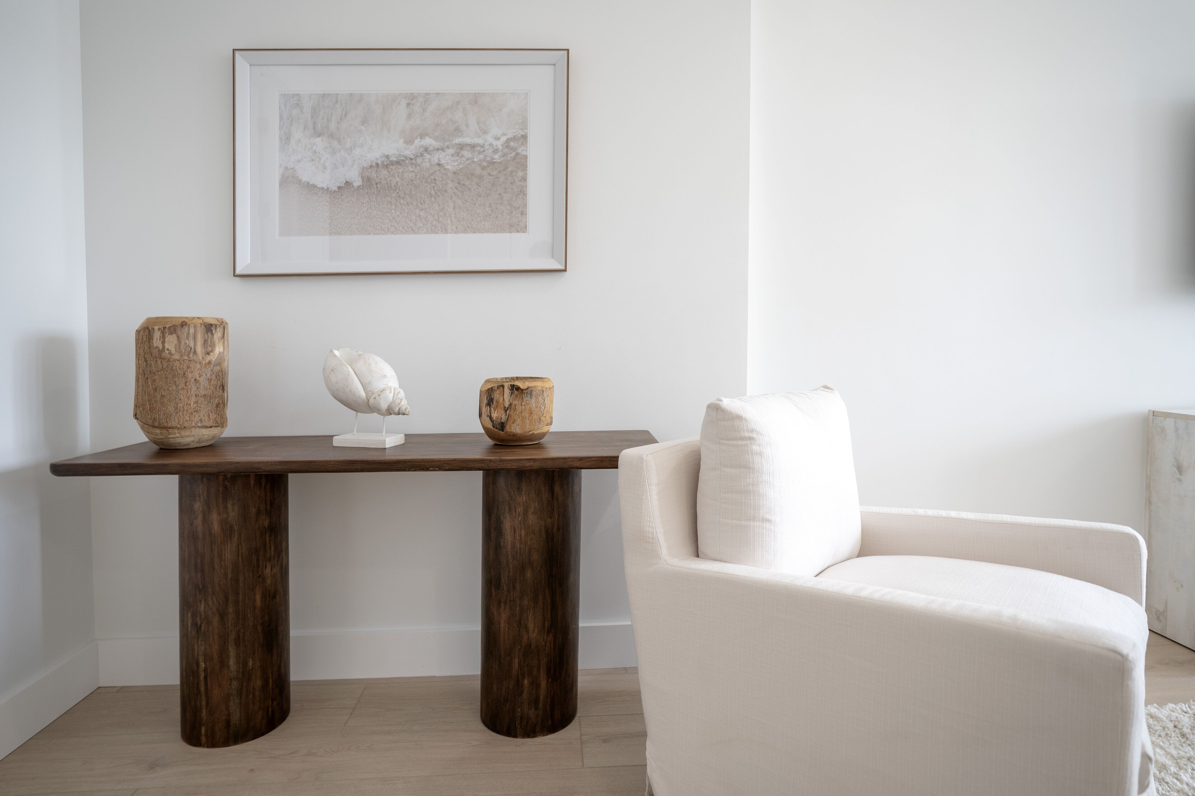 Een moderne woonkamer met een houten salontafel, een witte fauteuil en een lijstwerk abstract schilderij aan de muur.