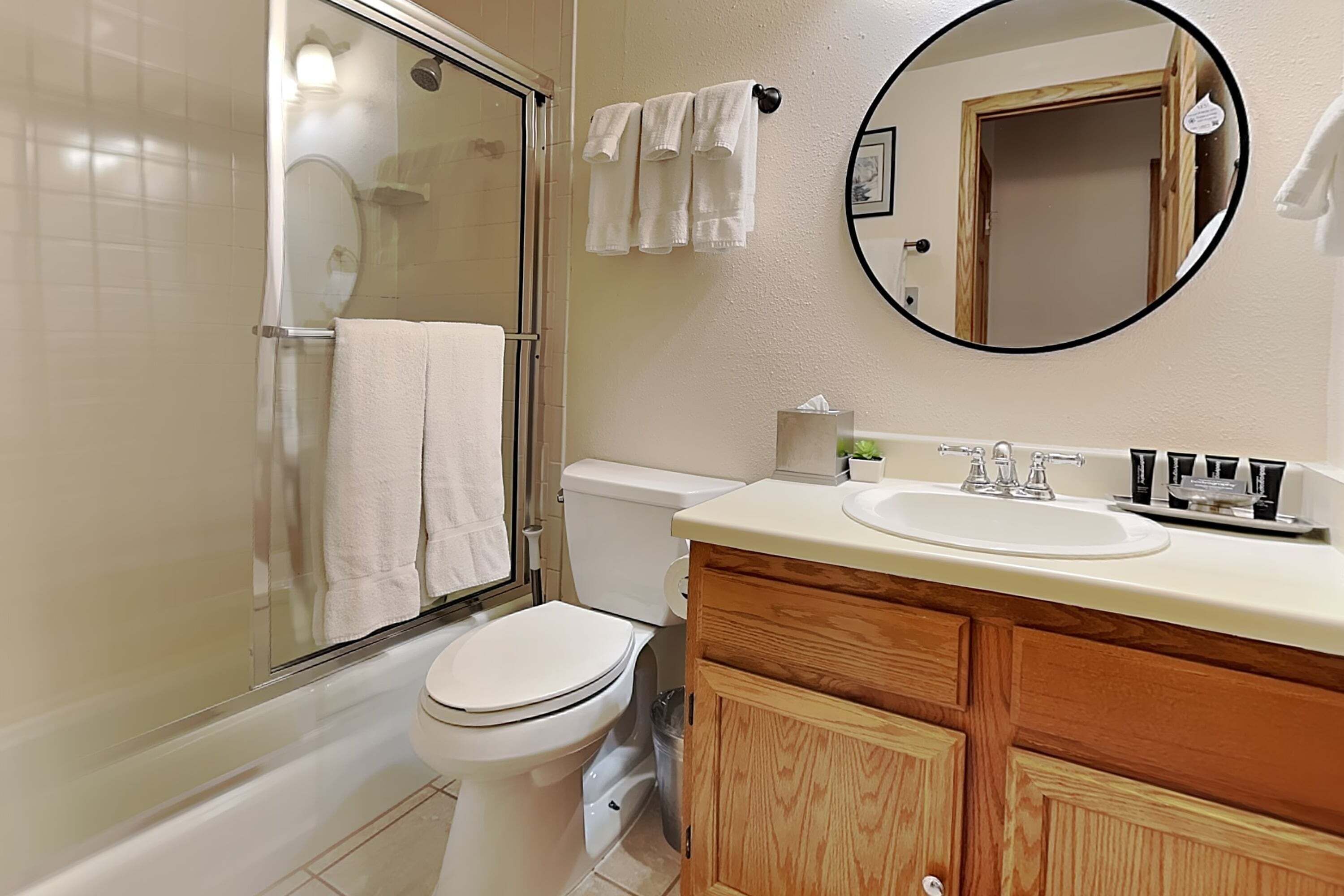 Un bagno con doccia vetro, WC, lavandino e specchio, corredato di articoli da toilette.