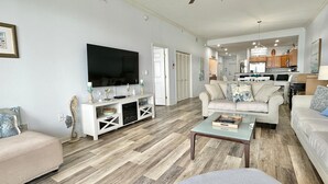 Ein geräumiges Wohnzimmer mit großem Fernseher, Kamin und einer Küche im Hintergrund.
