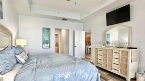 Ein Schlafzimmer mit einem Bett, einem Schminktisch, einem Fernseher und einem Flur, der zu einem Essbereich führt.