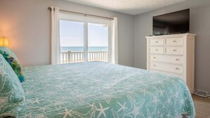 Quarto com cama, televisão em uma cômoda e vista para o oceano pela janela.
