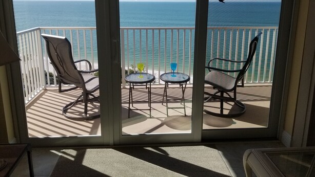 Un balcon avec deux chaises et une petite table, donnant sur une plage et l’océan.