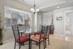 A dining area with a glass table, black chairs with red and yellow striped cushions, a sailboat decoration, and a chandelier. - Palisades 202E-2B - Three Bedroom Apartment, Sleeps 8 (Lake Ozark)