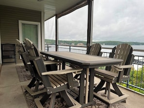 A covered outdoor area with a table and chairs, a view of a lake, and a railing. - Palisades 202E-2B - Three Bedroom Apartment, Sleeps 8 (Lake Ozark)