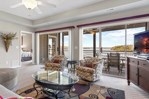 A spacious living area with a glass table, two patterned armchairs, a sofa, and a TV on a cabinet. - Palisades 202E-2B - Three Bedroom Apartment, Sleeps 8 (Lake Ozark)