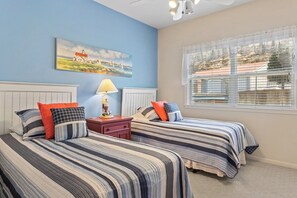 A bedroom with two beds, a nightstand, a lamp, a painting, and a window with blinds.