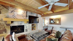 A cozy living room with a fireplace, leather sofas, a coffee table, and a ceiling fan. - 🌲Timberline B2A Deluxe 3-Bedroom ~Hot Tub~Pool~WiFi~Ski-in/out~Local Shuttle🌲 (Snowmass Village)