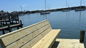 Una panchina di legno su un molo, con un'acqua calma e imbarcazioni sullo sfondo.