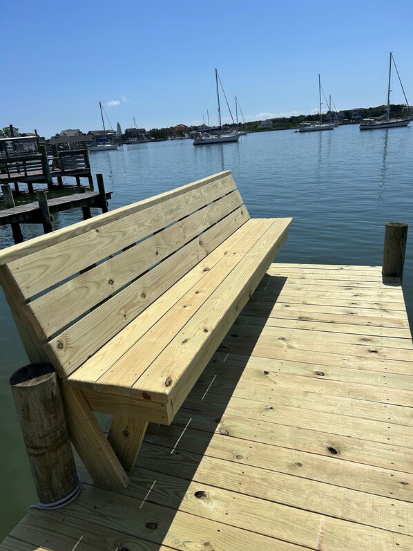 A wooden bench on a dock with a calm water body and boats in the background.