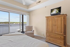Ein Schlafzimmer mit einem großen Bett, einem Holzschrank, einem Fernseher, einem Sessel und einem Balkon mit Blick aufs Wasser.