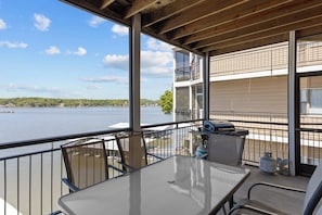 Ein Balkon mit Tisch und Stühlen, mit Blick auf ein Gewässer und eine entfernte Küstenlinie.
