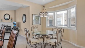 A dining area with a glass table, metal chairs, a chandelier, and a fireplace.