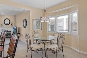 A dining area with a glass table, metal chairs, a chandelier, and a fireplace.
