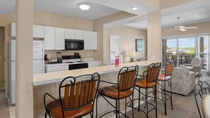 A modern kitchen with white cabinets, a black microwave, and a bar area with metal chairs.