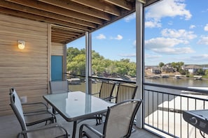 Ein Balkon mit Glastisch und Stühlen, der auf ein Gewässer und Gebäude mit Blick blickt.