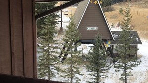 Vista des d'un balcó amb barana de fusta, amb una edifici amb la inscripció "CHAIR 3" i un paisatge cobert de neu i arbres al fons.