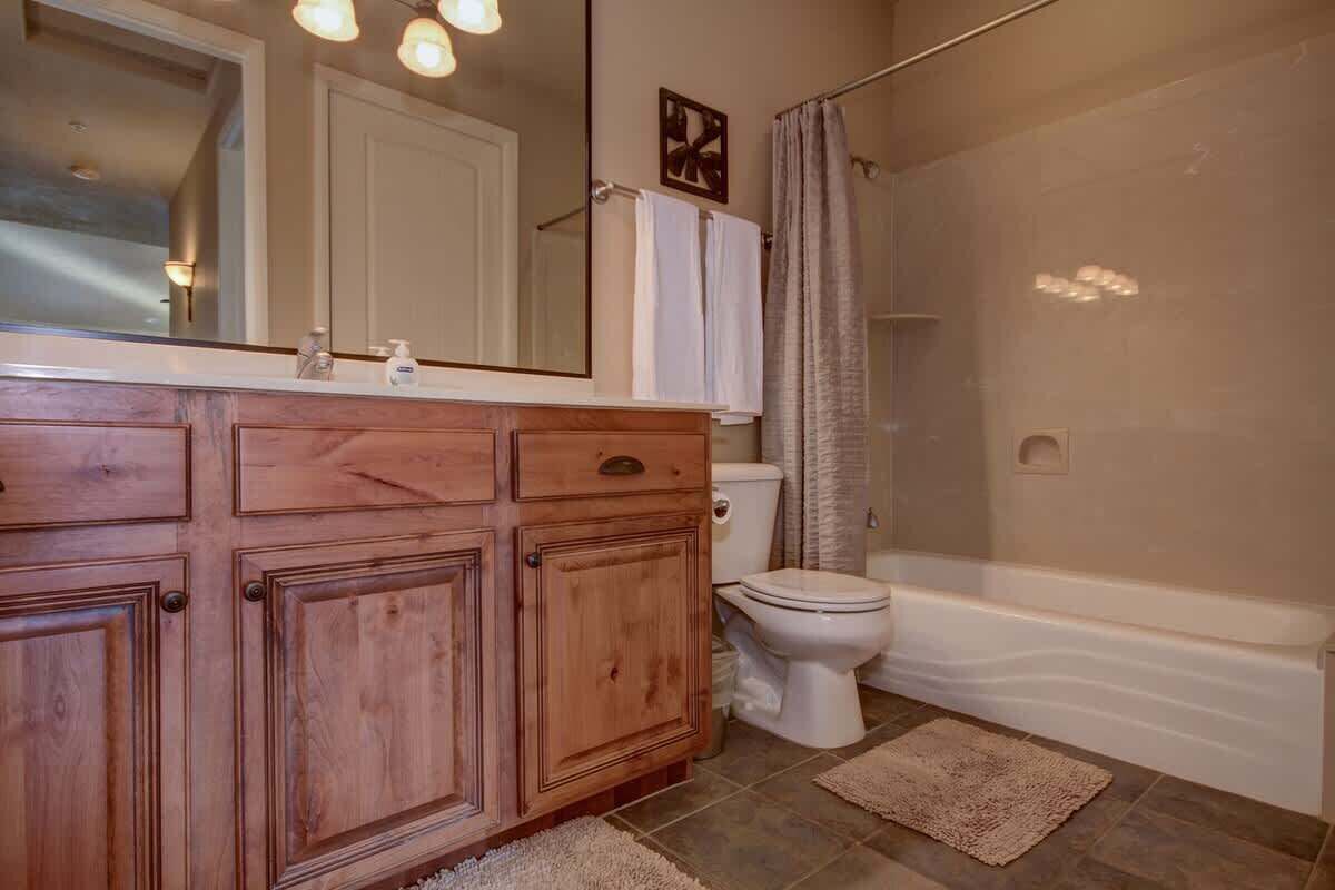 Un baño con armarios de madera, inodoro, bañera y cortina de ducha.