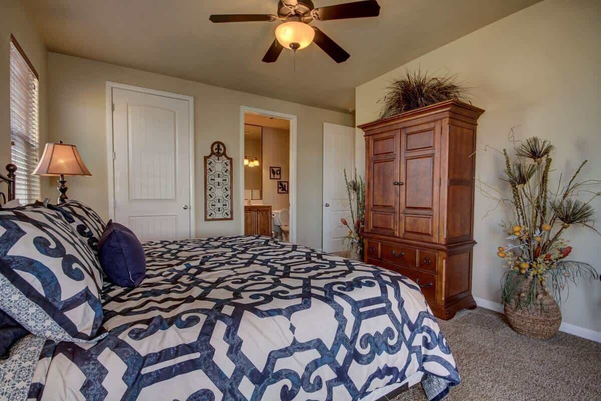 A bedroom with a bed, a ceiling fan, a wooden cabinet, and a door leading to another room.