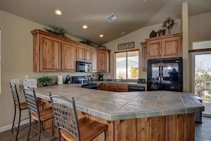 Una cocina con armarios de madera, una isla grande con taburetes de bar, un refrigerador y una ventana con persianas.