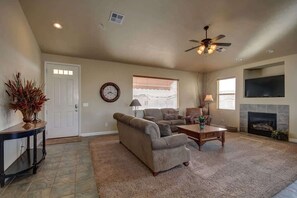 A living room with a sofa, armchairs, a coffee table, a fireplace, a television, and a ceiling fan.
