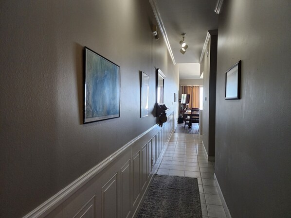 A hallway with a tiled floor, a dark rug, and framed artwork on the walls.