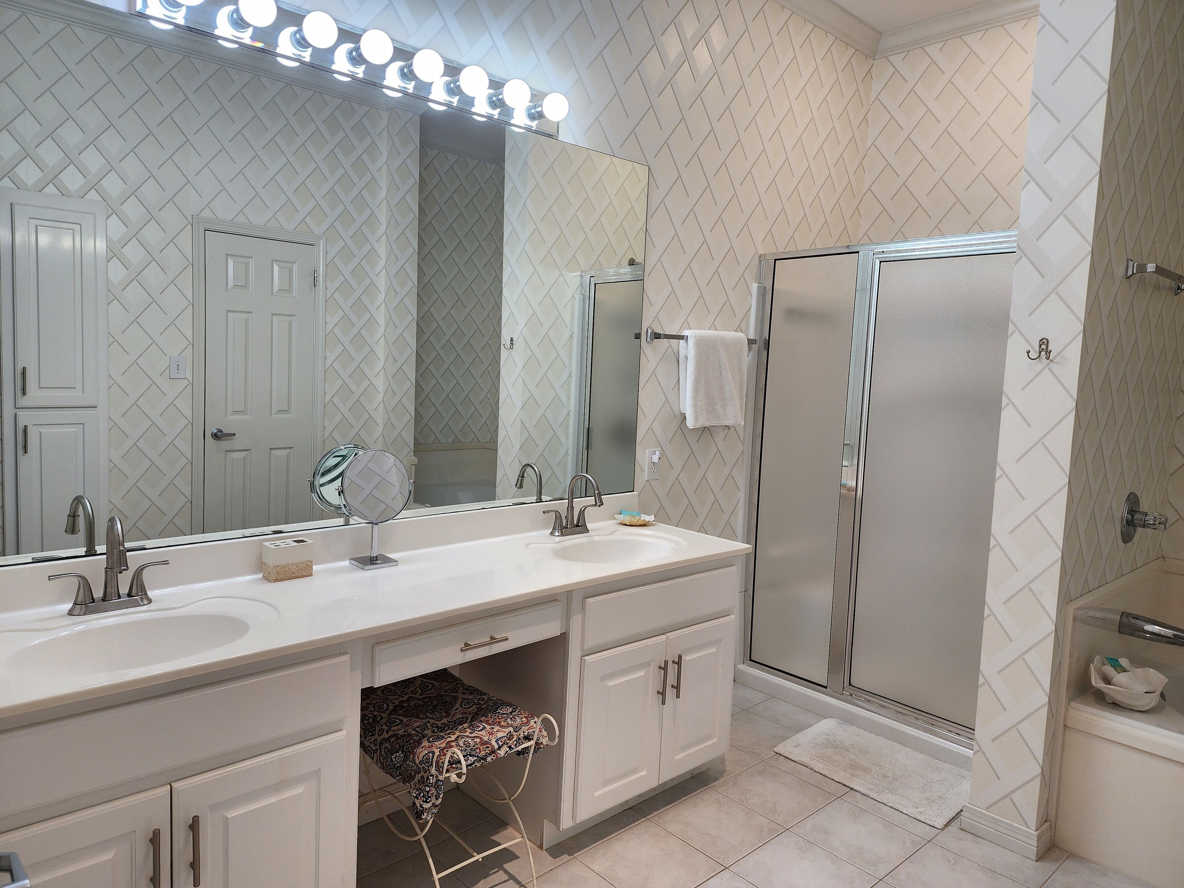 A bathroom with a vanity, a large mirror, a shower, and a towel rack.
