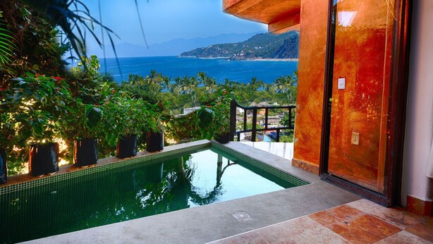 A pool with a view of the ocean and mountains, surrounded by lush greenery and a modern building facade. - Private Dipping Pool. Ocean Views. (Casita #4) (Sayulita)