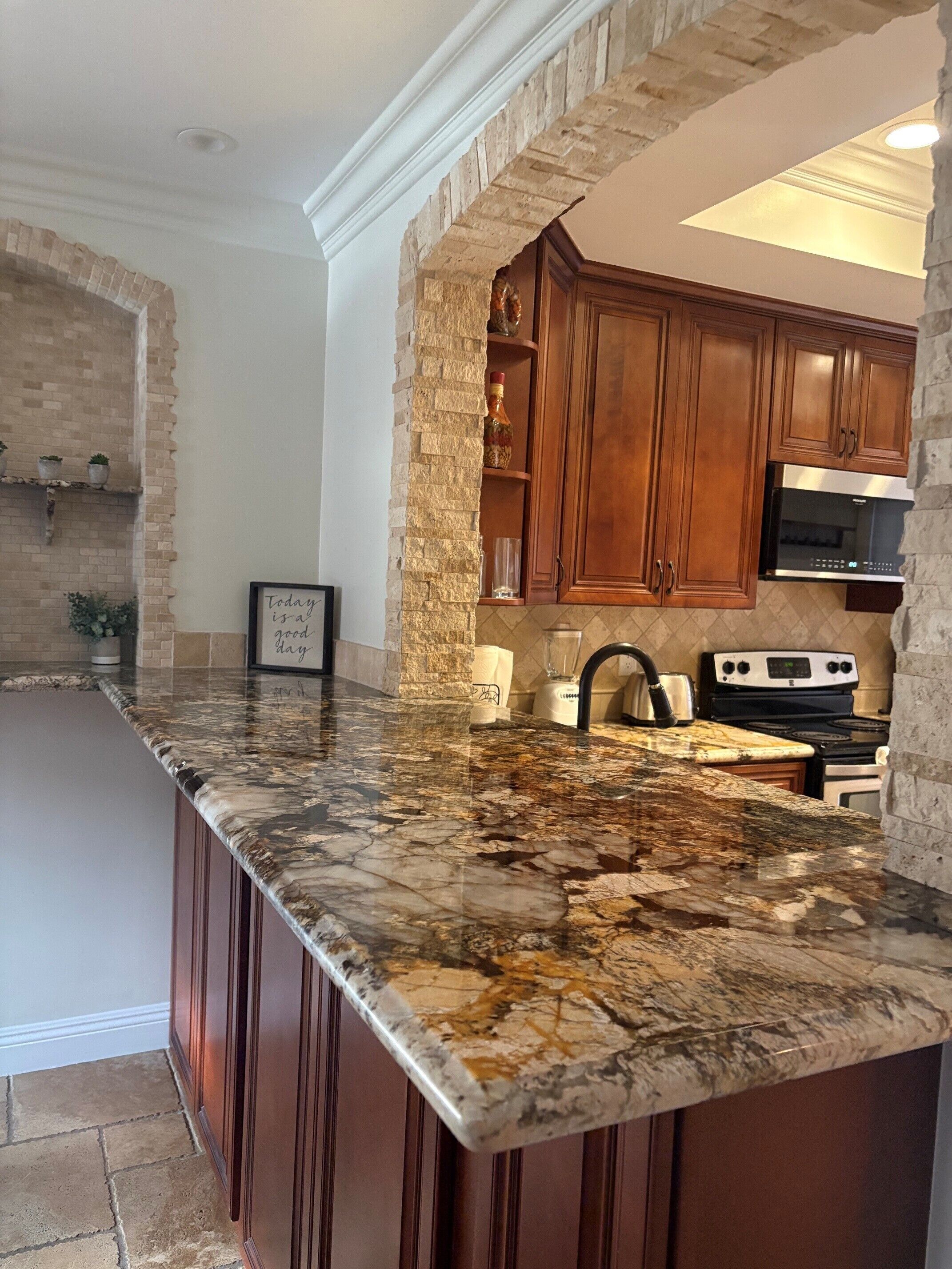 A kitchen with a granite countertop, wooden cabinets, a built-in oven, and a stone accent wall.