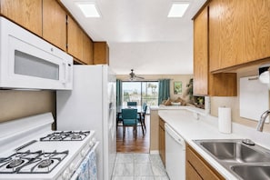 A kitchen with a stove, microwave, and sink, leading to a dining area with a table and chairs.