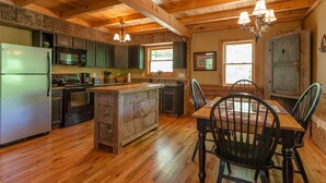 Una cocina rústica con vigas de madera, una isla central y un comedor con sillas y una mesa.