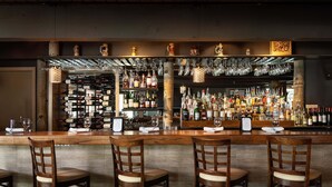 Un espace bar avec des chaises en bois, un comptoir avec des verres et des bouteilles, et un mur entièrement recouvert de bouteilles de vin.