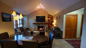 A cozy living room with a fireplace, a dining area, and a TV mounted on the wall.