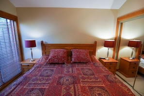 Ein Schlafzimmer mit einem großen Bett, zwei Nachttischen, einem Spiegel und einem Fenster mit Jalousien.
