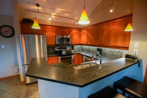 A modern kitchen with stainless steel appliances, wooden cabinets, and pendant lighting. - The Woods - Renovated, Family Friendly Condo on Free Shuttle and Golf Course (Whistler)