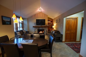 Ein gemütliches Wohnzimmer mit Kamin, Essbereich mit Tisch und Stühlen sowie einem an der Wand montierten Fernseher.