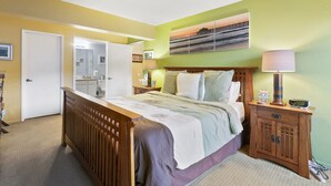 A bedroom with a bed, bedside tables, a nightstand, a mirror, a door, and a painting on the wall. - C54: 2 Bedroom, 2 Bath Condo, Balcony with Views, Pool, BBQ (Avalon)