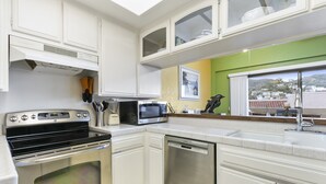 A modern kitchen with white cabinets, stainless steel appliances, and a view of the city through a window. - C54: 2 Bedroom, 2 Bath Condo, Balcony with Views, Pool, BBQ (Avalon)