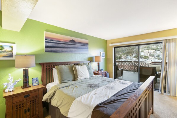 A hotel room with a bed, two bedside tables, a nightstand, a balcony with a view of a cityscape.