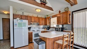 Eine Küche mit Holzausstattung, einem weißen Kühlschrank, einem Herd, einer Mikrowelle und einer Bar mit Hockern.