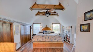 Ein Schlafzimmer mit einem großen Bett, Holzbalken an der Decke, einem Deckenventilator, einem Bücherregal und einem Fenster.