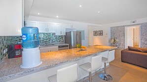 Une cuisine moderne avec des meubles blancs, un plan de travail en granit et un distributeur d’eau.